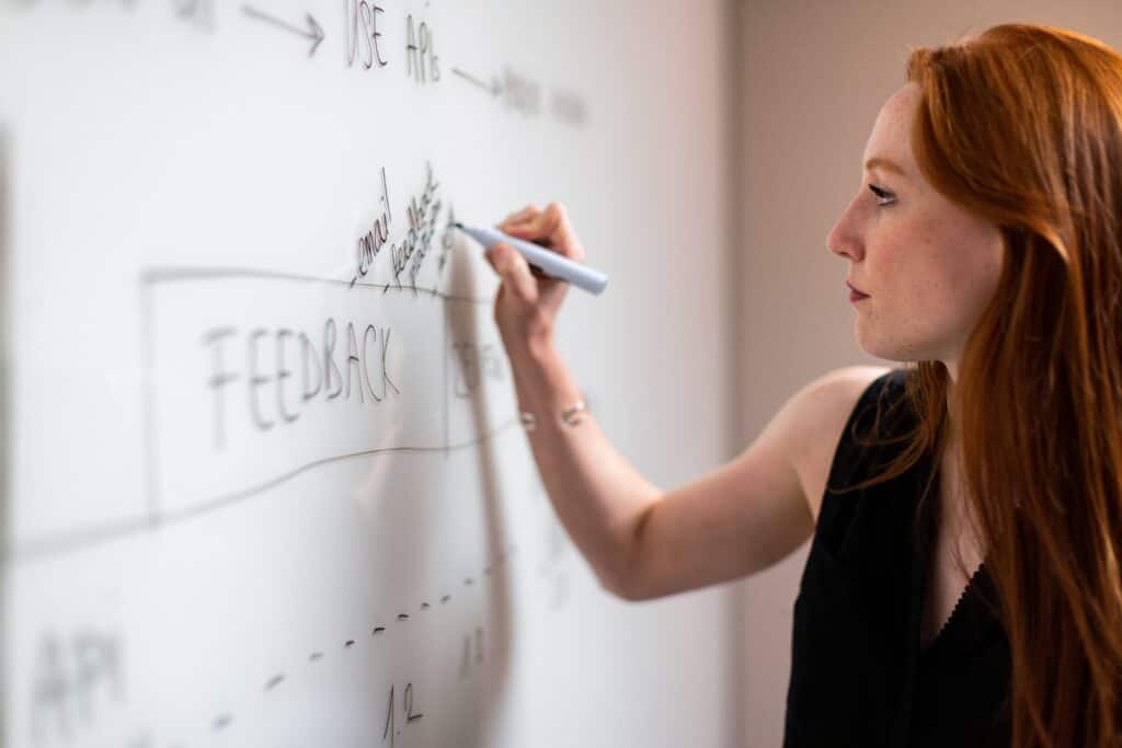 Woman writing on a whiteboard, and the word 'feedback' is seen.