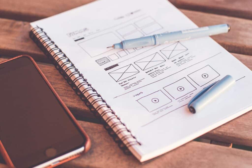 A notepad and pen, with a wireframe design in progress